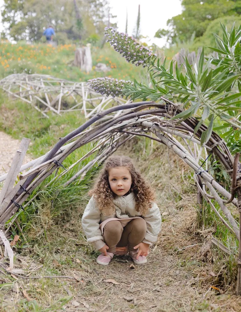 Little girl sitting under stick fort