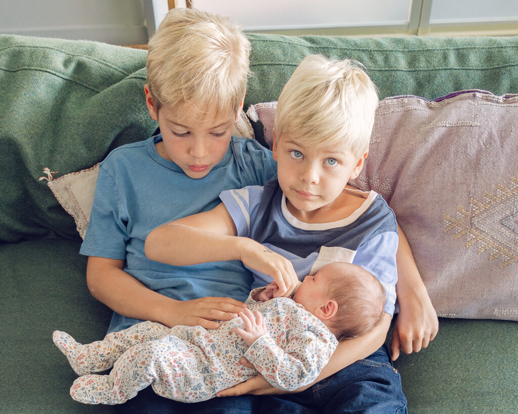 Two older brothers holding baby sister during At Home newborn photos in Berkeley, California