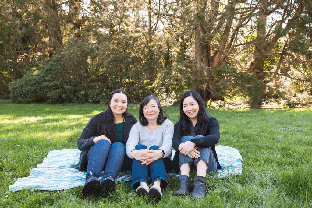 Mother and her two daughters sitting in the grass on a blanket 