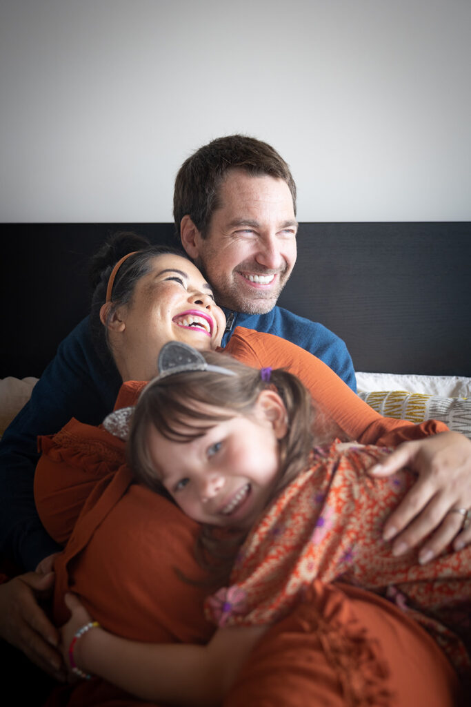 Family of three laying on a bed during an at home maternity session in the Bay Area