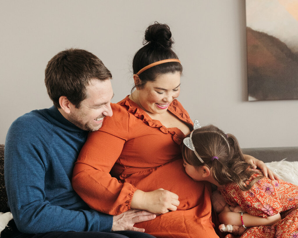 Family of three sitting on a couch during their at home maternity session in the Bay Area