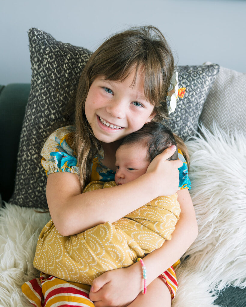 Big sister holding her newborn sister during at home newborn session in the Bay Area