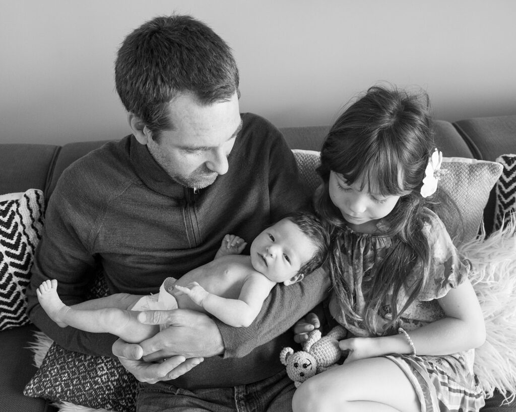 Black and white photo of father, newborn daughter, and older sister during at home newborn session