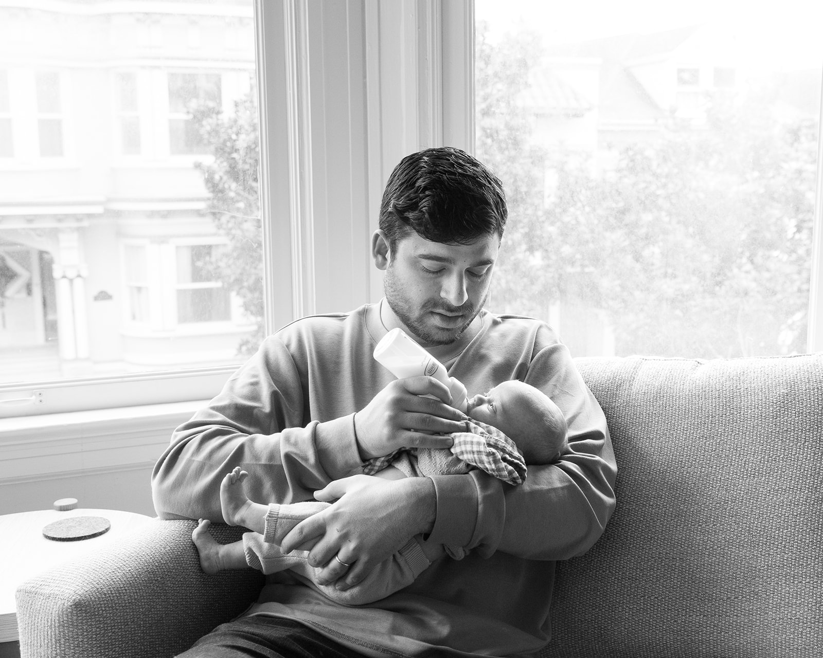 Black and white photo of a father feeding his newborn during their lifestyle at-home San Francisco newborn photoshoot