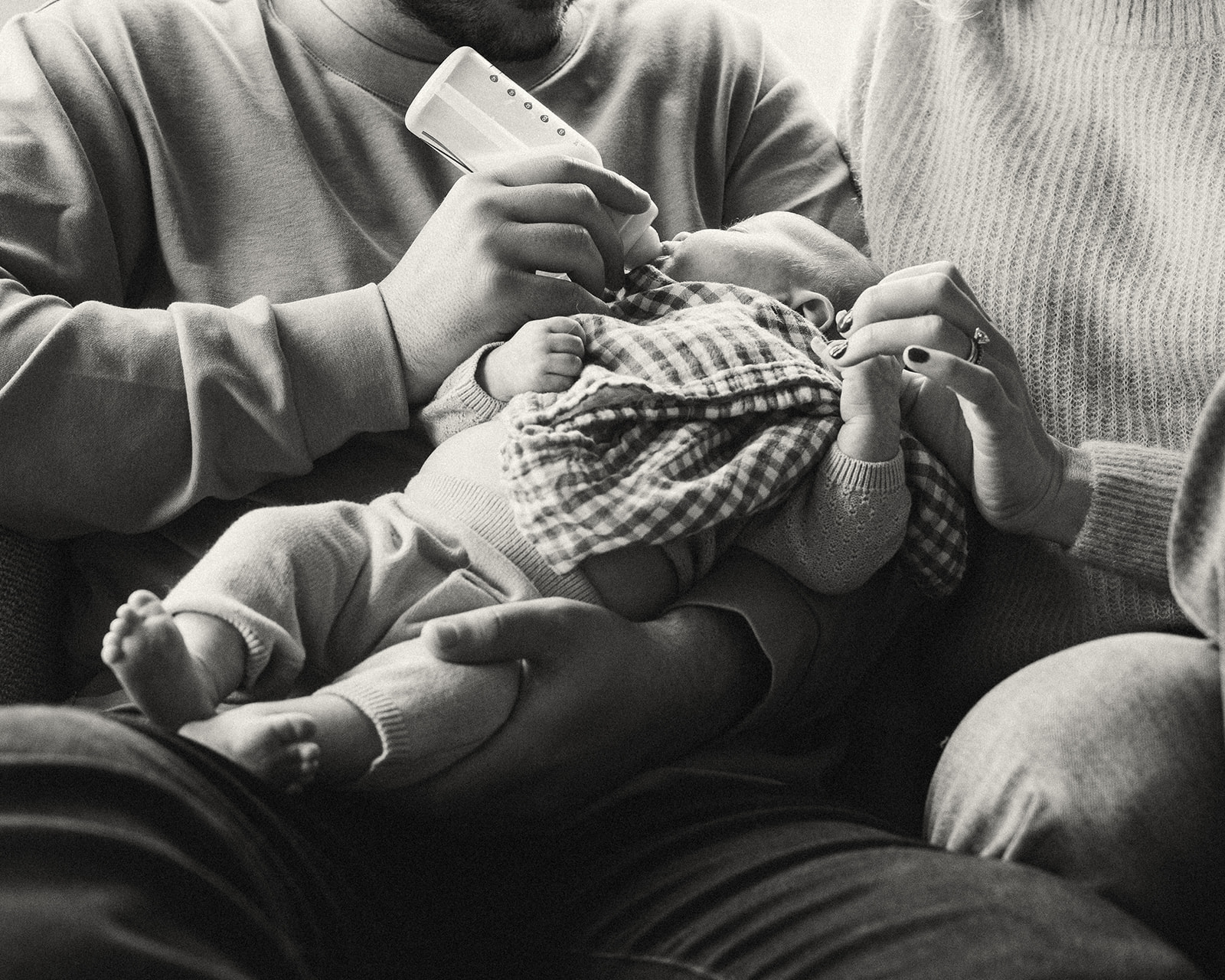 Black and white photo of a father feeding his newborn during their lifestyle at-home San Francisco newborn photoshoot