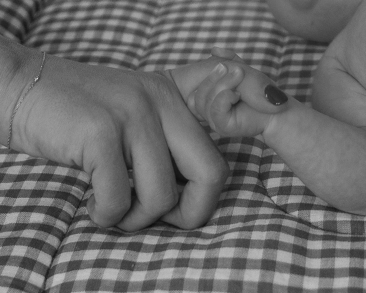 Black and white photo of a newborn holding his mothers finger