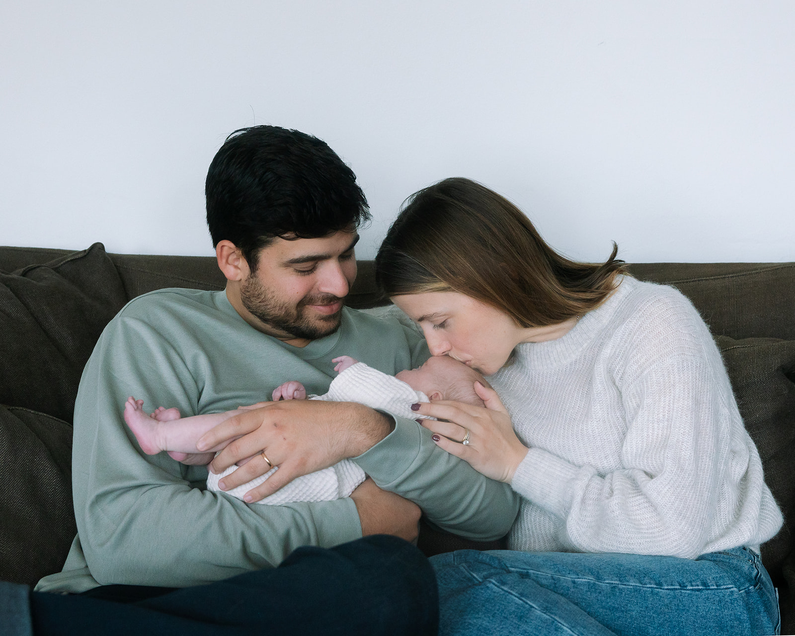 Mother and father sitting on their couch with their newborn baby