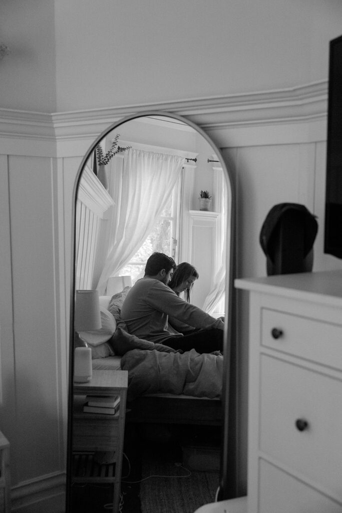 Photo of the reflection of a couple in a mirror as they sit on their bed