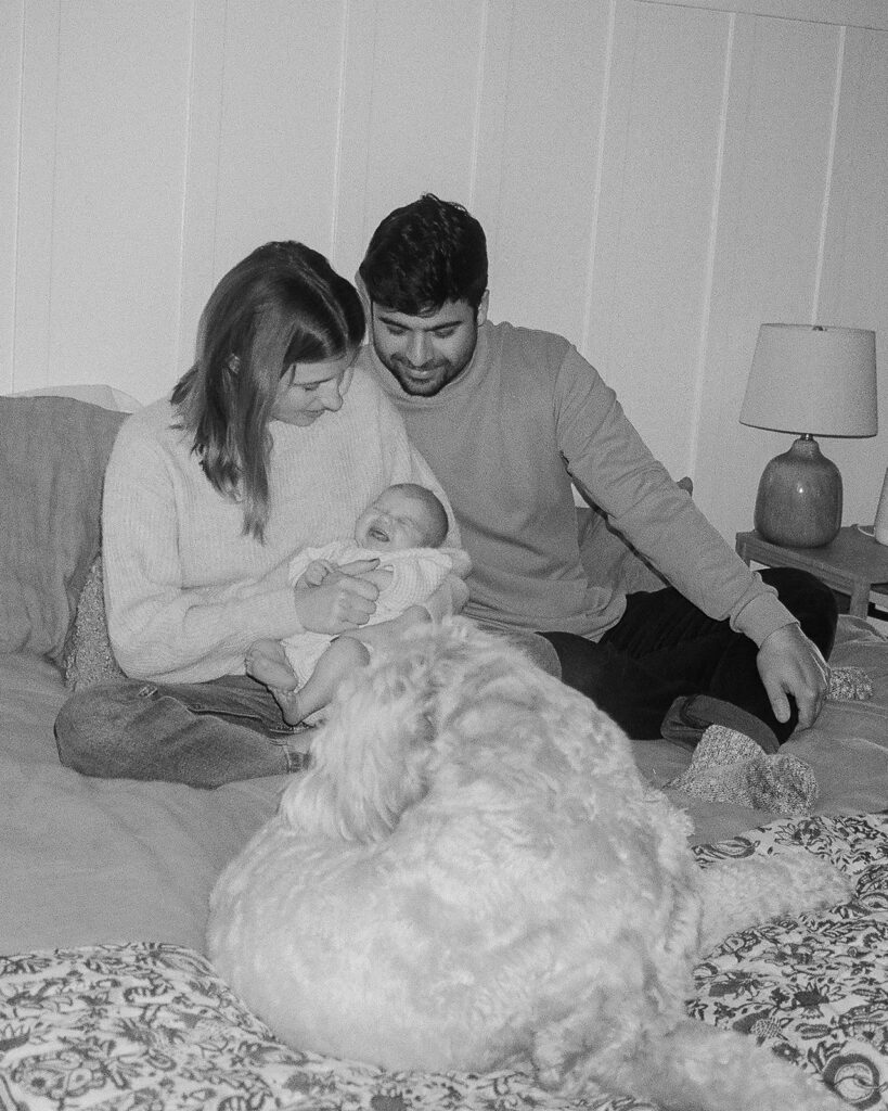 Mother, father, and family dog laying on a bed with their newborn baby on 35mm film