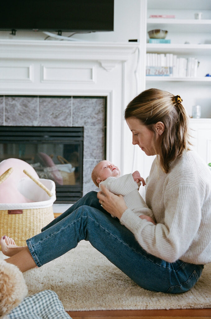 Mother sitting on the floor of her living room as she holds her newborn baby