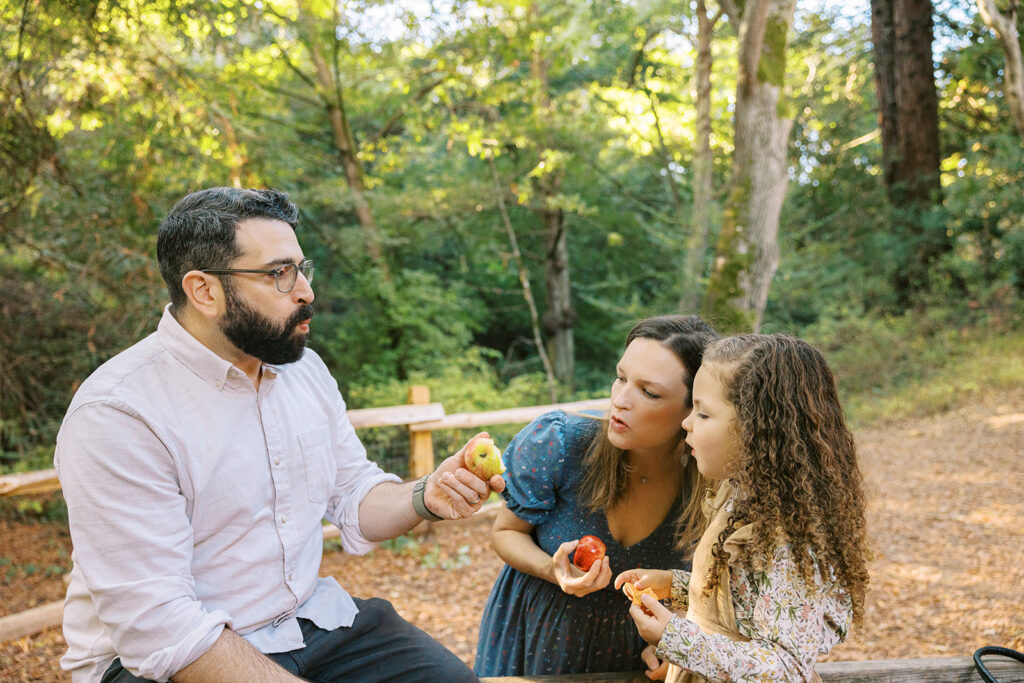 Little girl and her parents eating snacks at Tilden Regional Park in Berkeley, CA during their maternity & family pictures