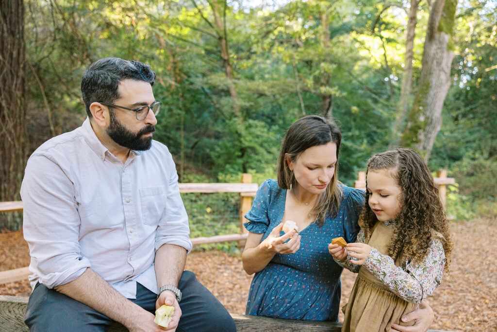 Little girl and her parents eating snacks at Tilden Regional Park in Berkeley, CA during their maternity & family pictures