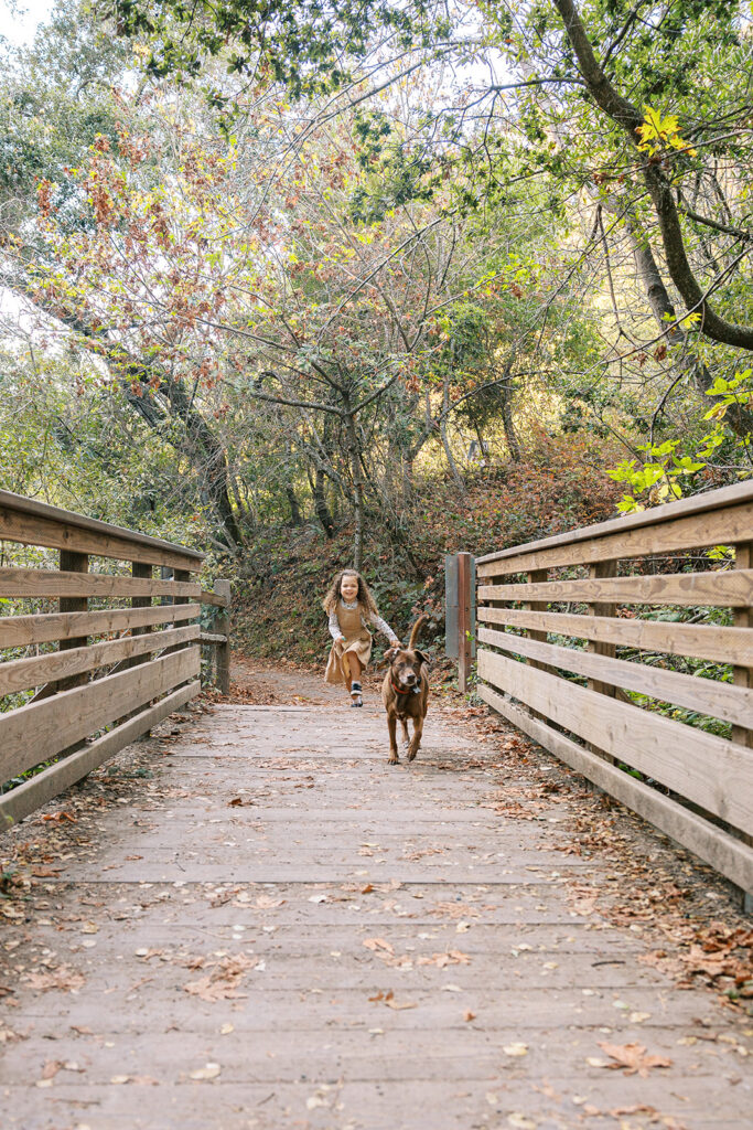 Little girl running along a bridge with her dog in Tilden Regional Park of Berkeley, CA