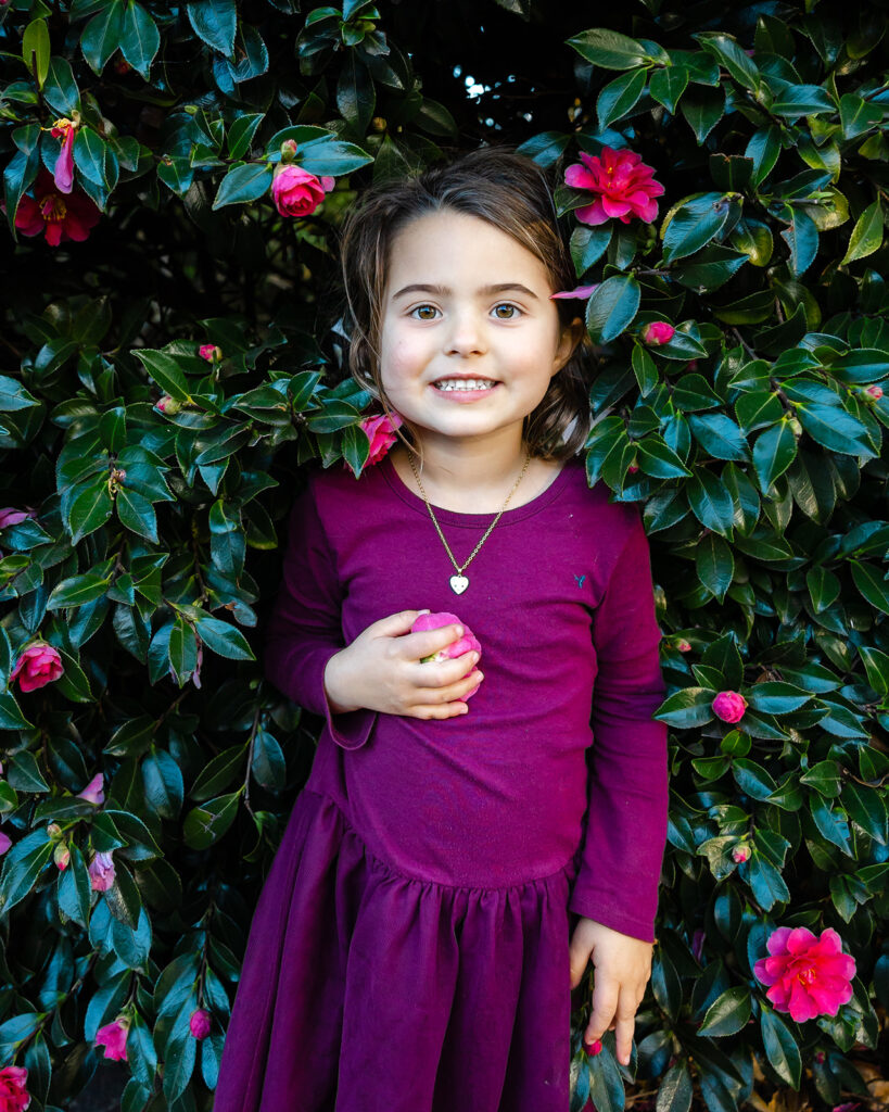 Little girl posing for photos in front of a flower bush
