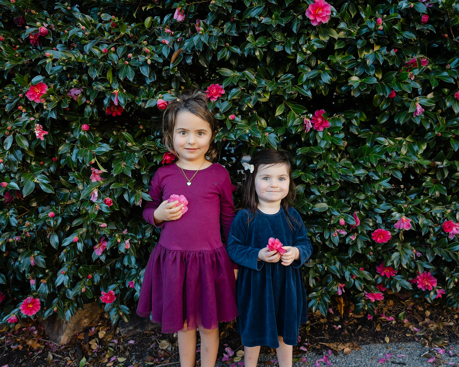 Little girls posing in front of a flower bush 