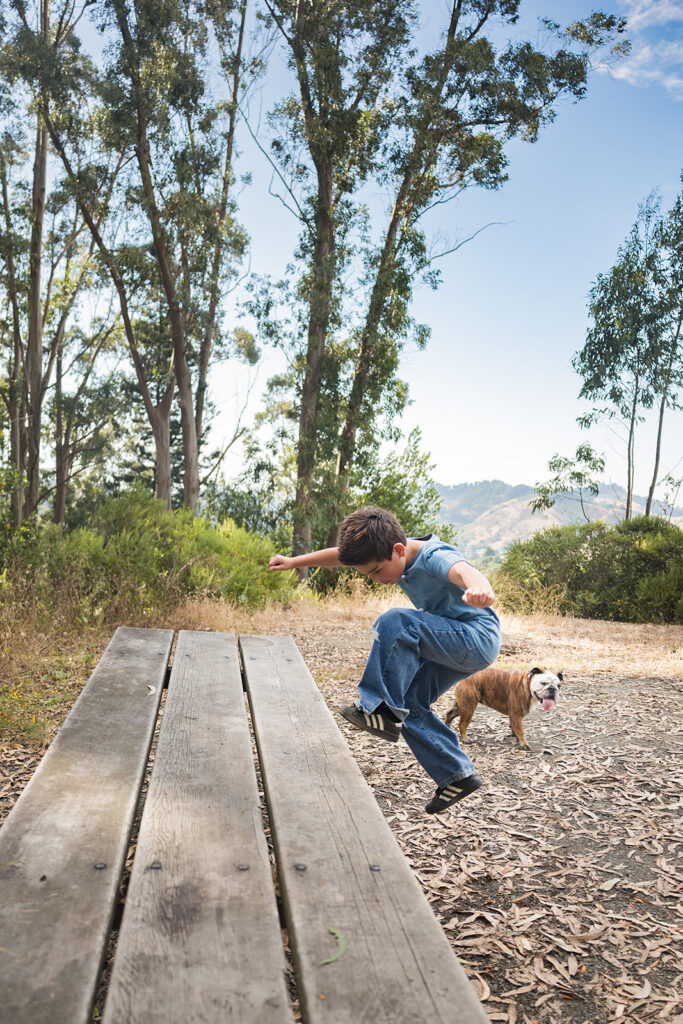 Young boy jumping on a bench with his dog nearby