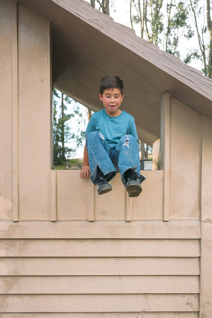 Little boy about to jump off of a in a light brown park building structure