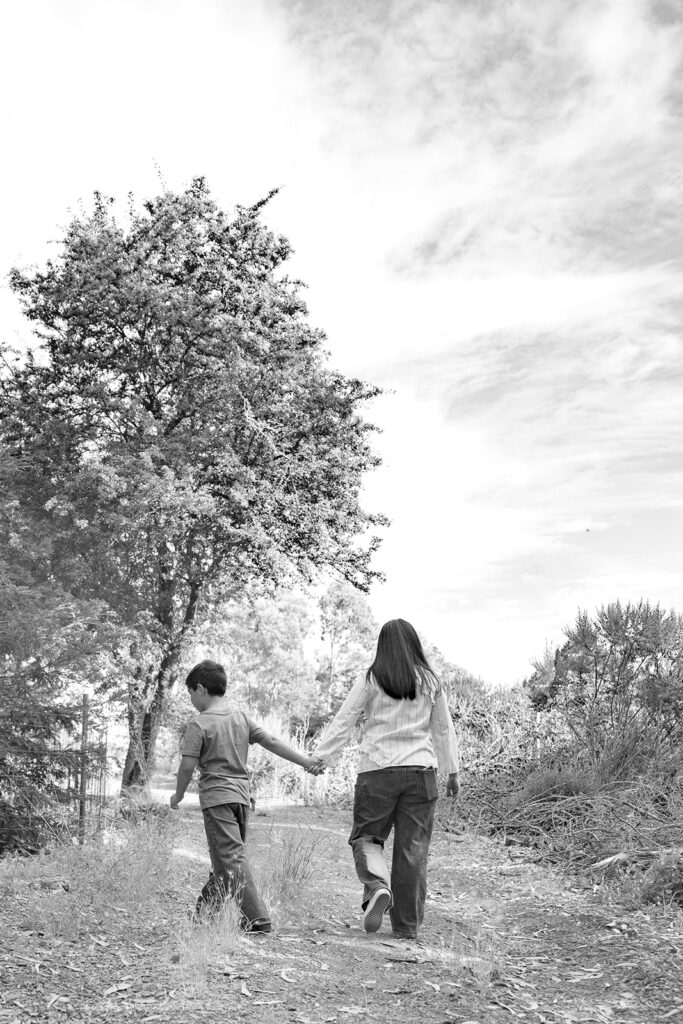 Black and white photo of a mother and son holding hands as they walk away from the camera