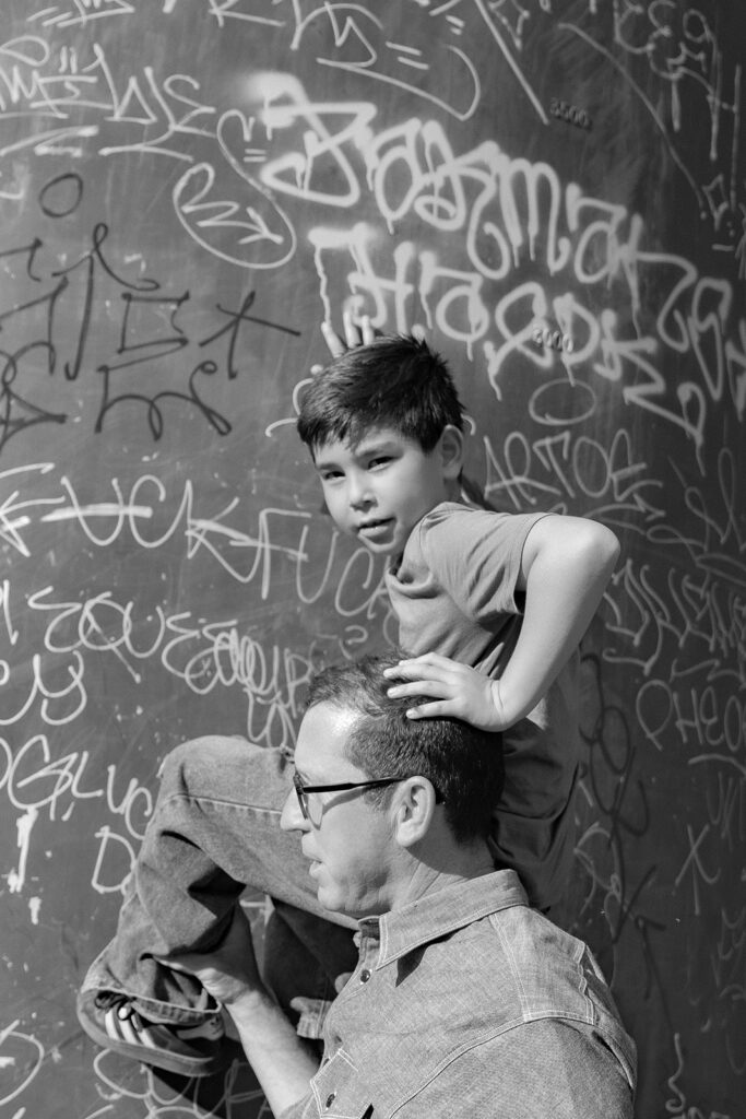 Black and white photo of a man holding up his son to check out the graffiti at Sibley Regional Park during their Oakland CA family photos