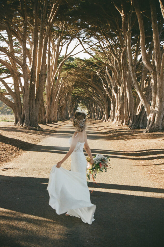 Woman standing in the Cypress Tree Tunnel wearing a wedding dress and holding her bouquet during her intimate Point Reyes elopement