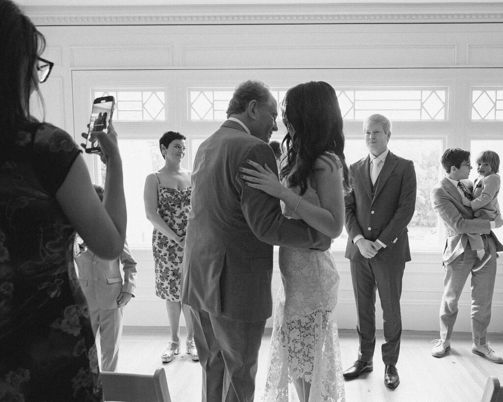 Black and white photo of a bride giving her dad a hug at the end of the aisle