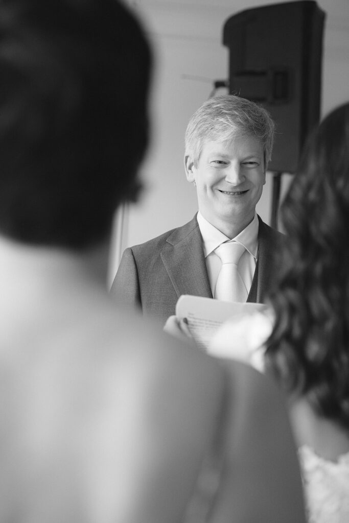 Black and white photo of a groom smiling during vow reading