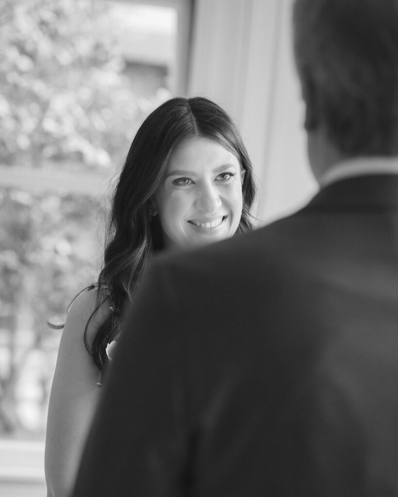 Black and white photo of a bride smiling at the groom during their intimate wedding ceremony