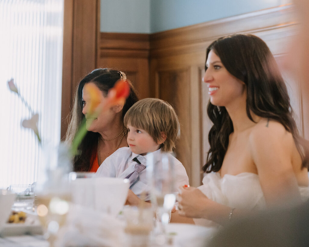 Bride smiling as guests give speeches during her wedding reception