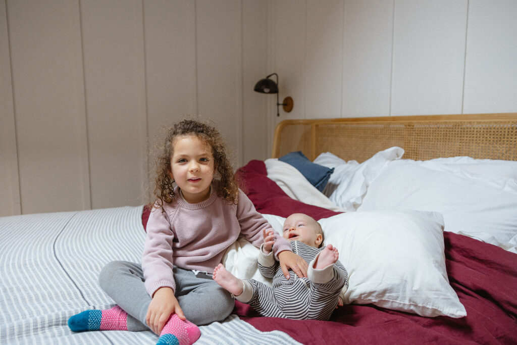 Young girl sitting on a bed next to her newborn sister