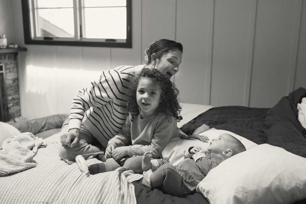 Black and white candid photo of a mother and her two daughters sitting on a bed 