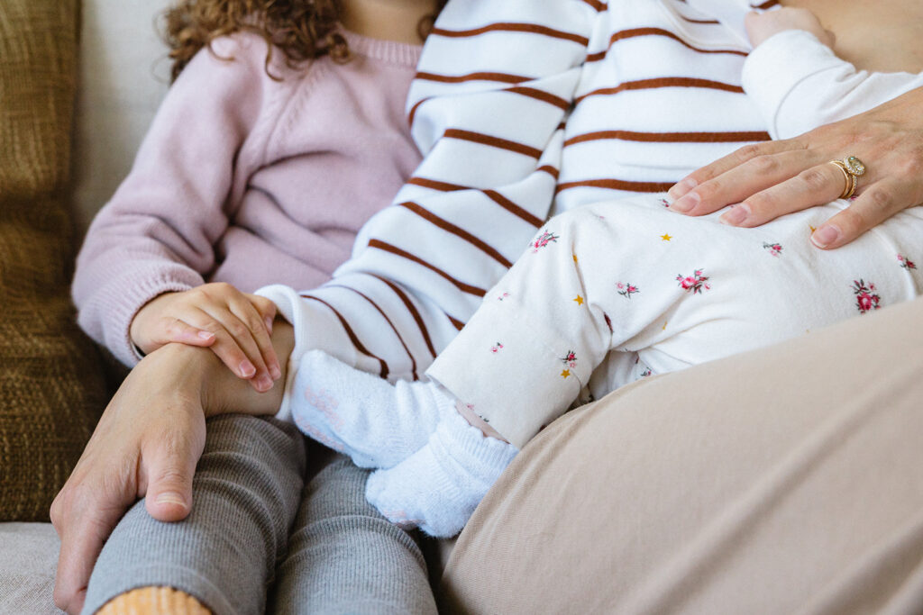 Mother and her two daughters sitting on a couch for their at-home newborn photos in Berkeley, California