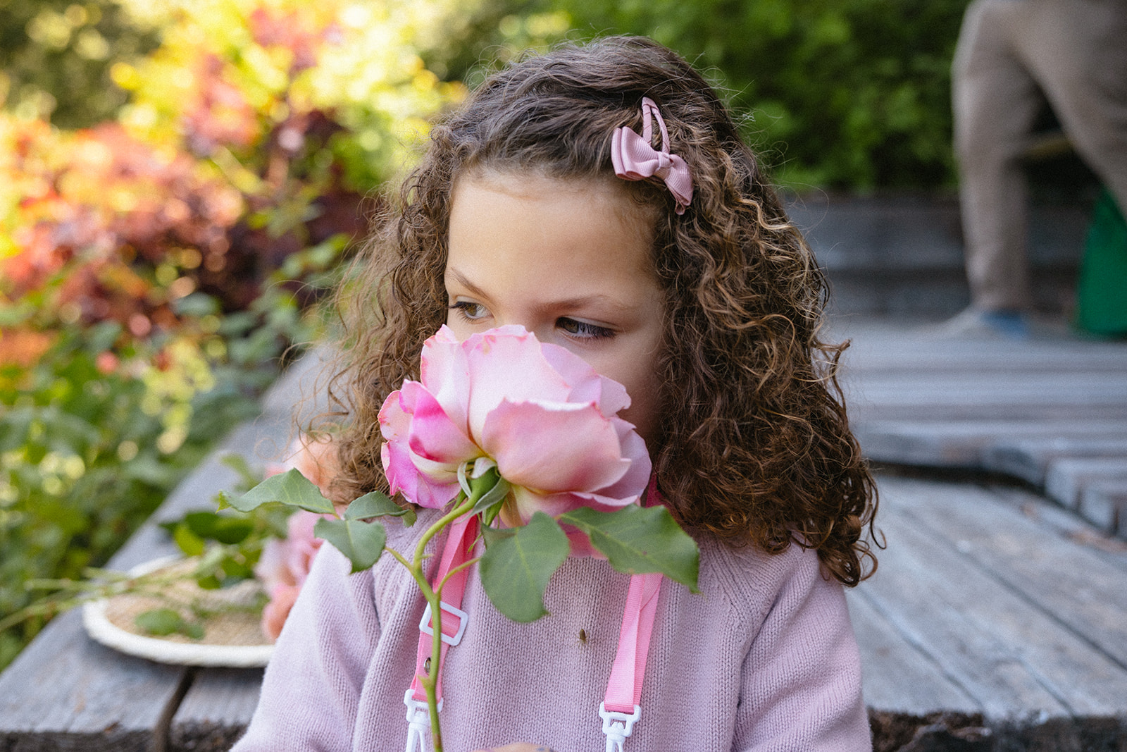 Little girl smelling a pink flower from her garden