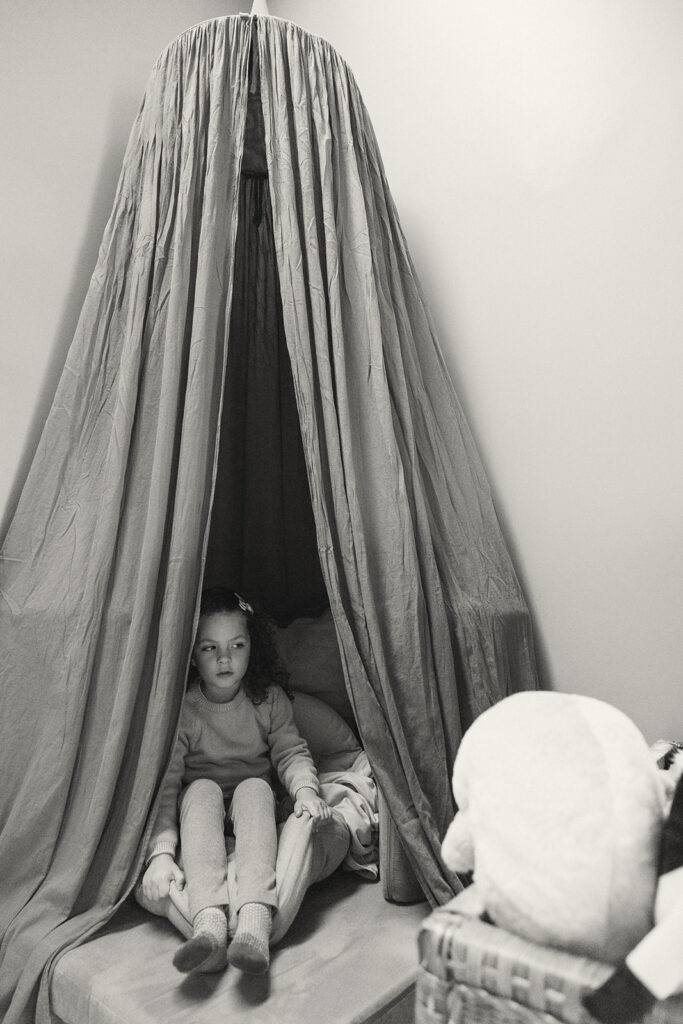 Black and white photo of a little girl sitting in a bedroom fort