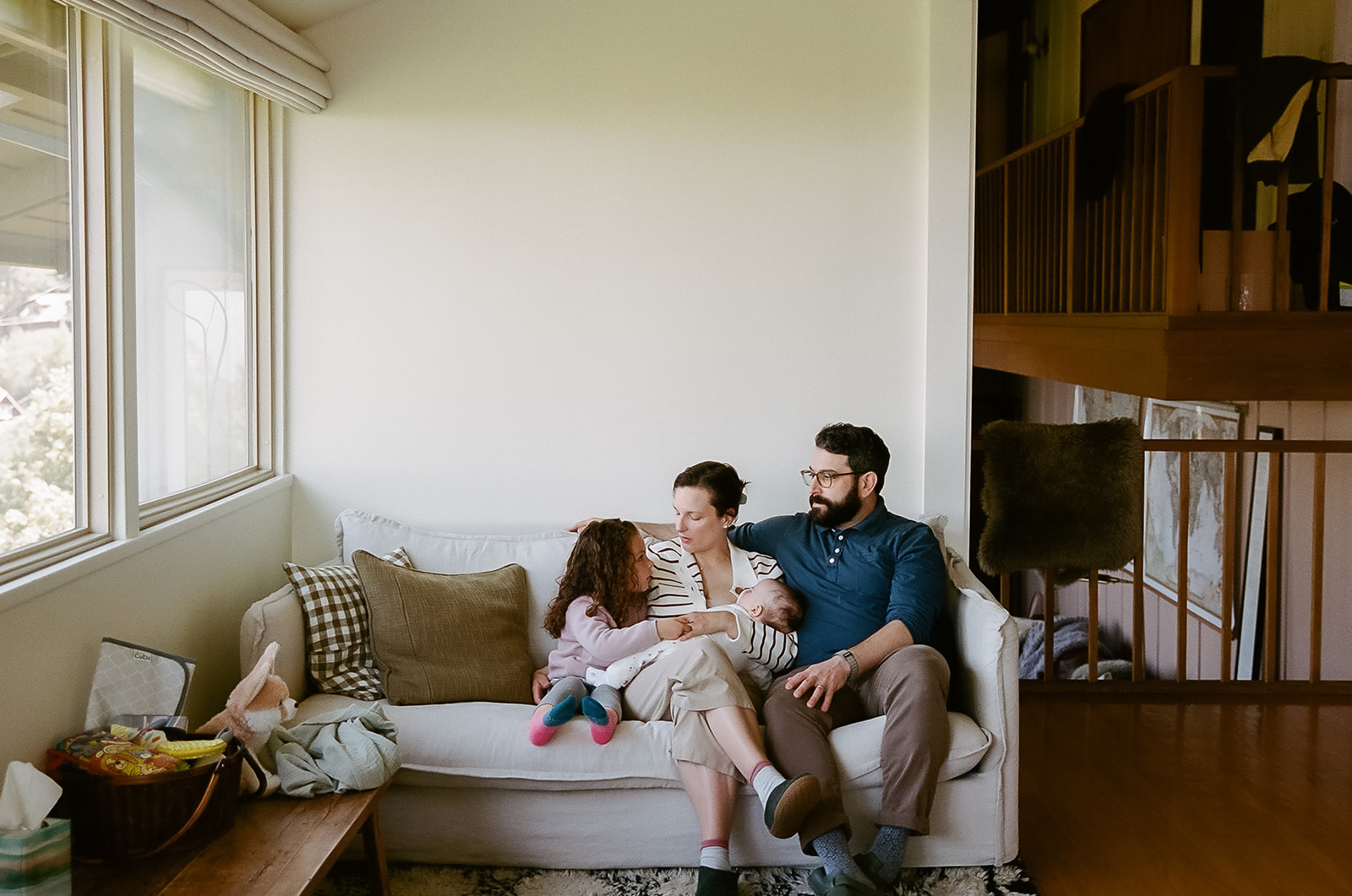 Family of four sitting on a couch during their at-home newborn photos in Berkeley, California