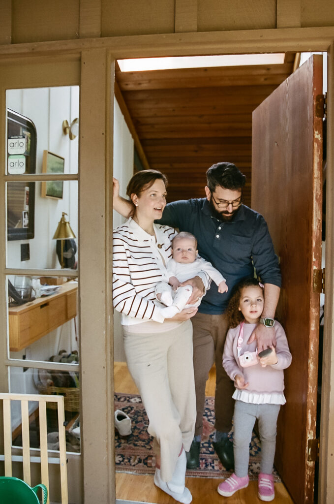 Family of four posing for photos at their front door as they say goodbye to the photographer after their at-home newborn family photos in Berkeley