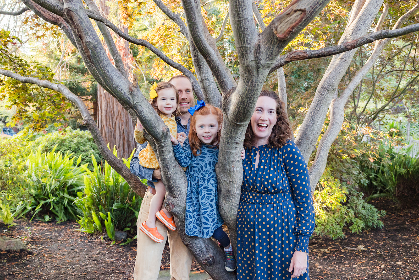 Family of four posing with a tree for their outdoor Piedmont Park family photos in the East Bay