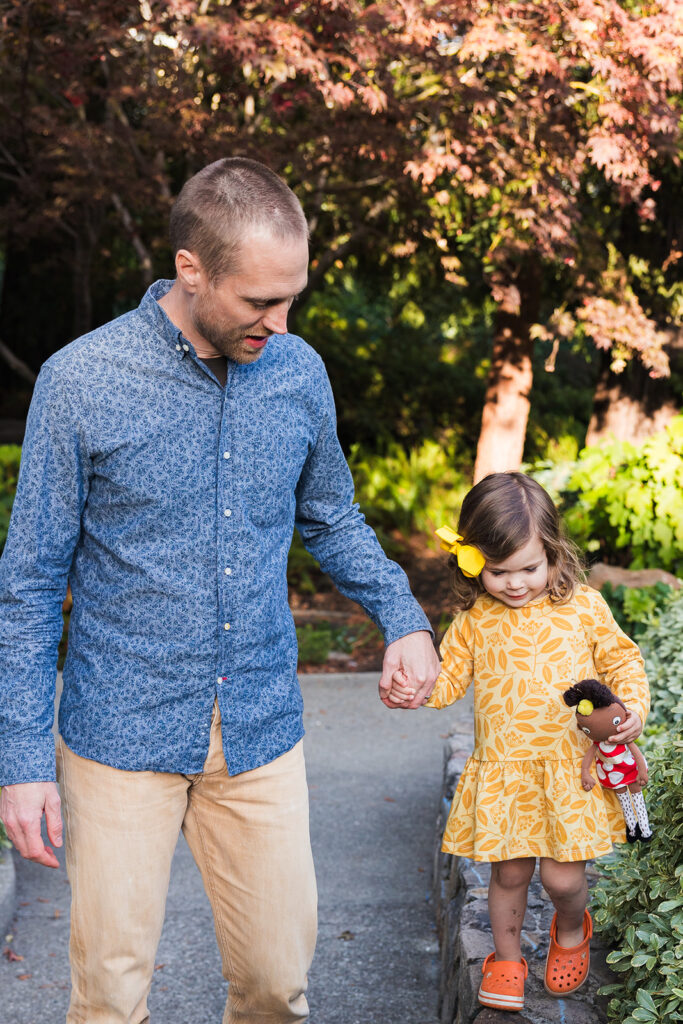 Father holding his daughters hand as she walks a brick sidewall