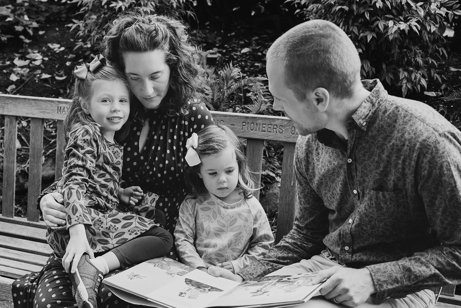 Black and white photo of parents reading a book to their two little girls