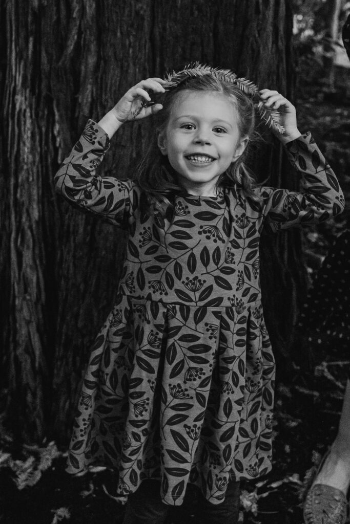 Black and white photo of a girl putting a plant crown on her head