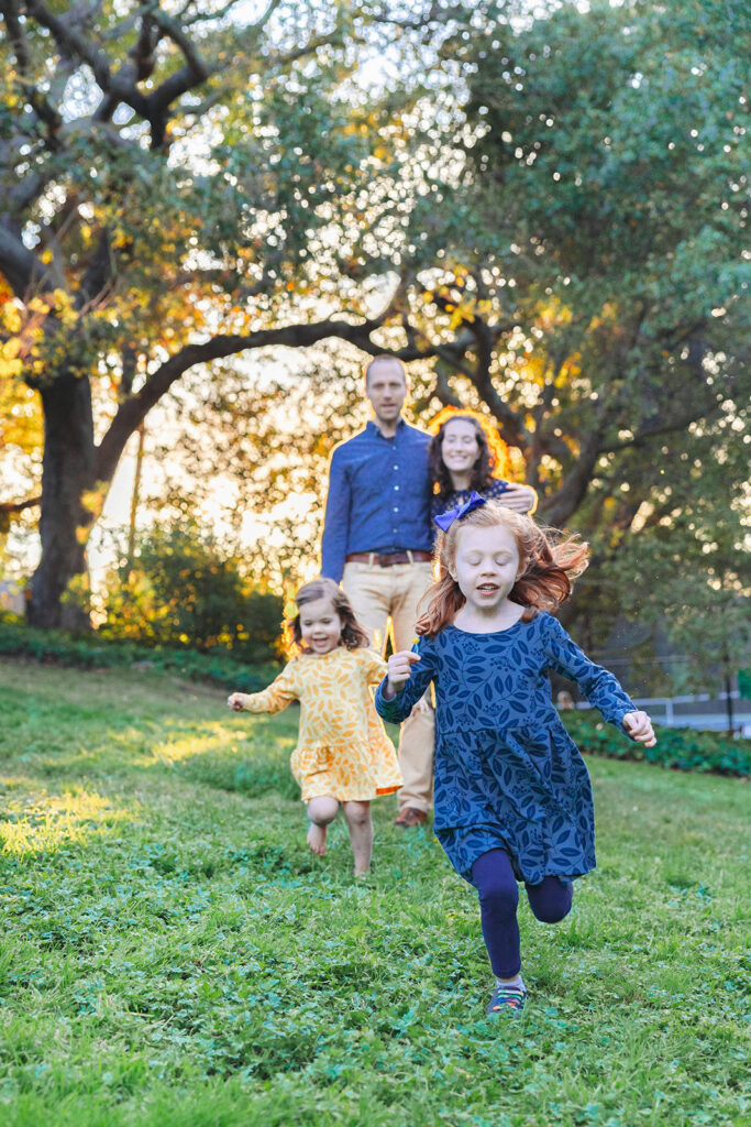 Two little girls running at Piedmont Park in the East Bay of California with their parents watching behind them.