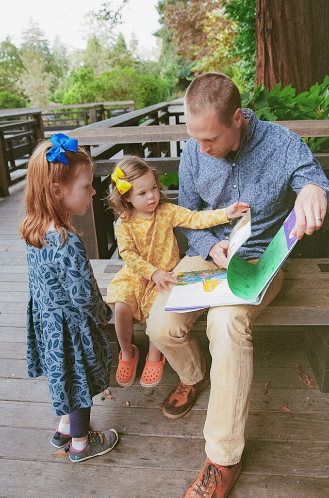 Father sitting on a park bench and reading is two daughters a book captured on 35mm film.