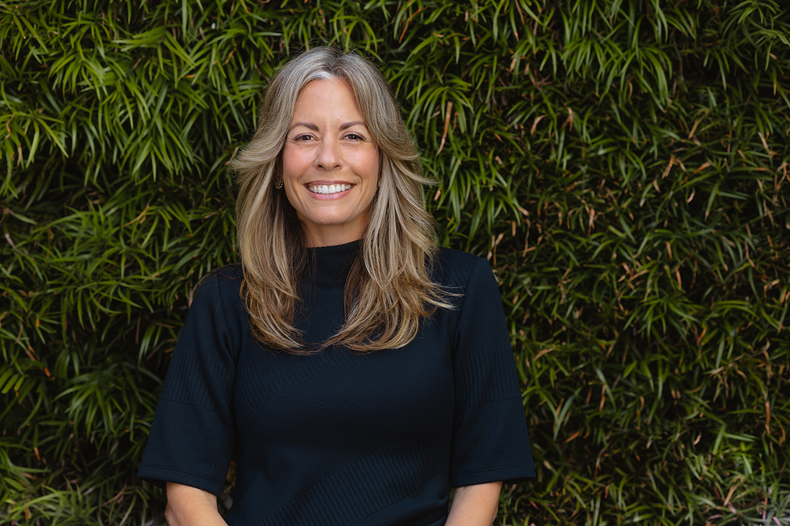 Woman posing in front of a green shrub bush