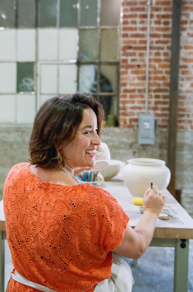 Woman looking behind her and smiling while painting her pottery