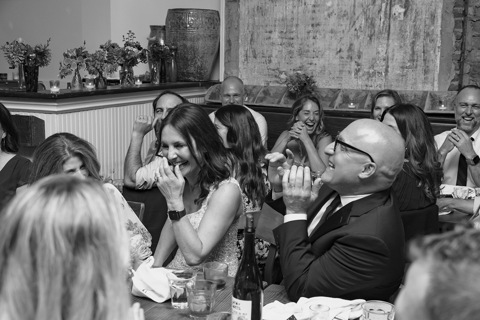 Black and white candid wedding reception photo of a bride and groom laughing during speeches