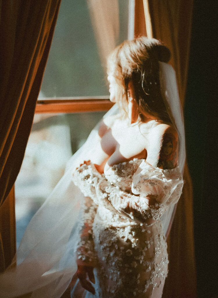 Bride standing by window in soft light on film at Nevada City wedding getting ready.