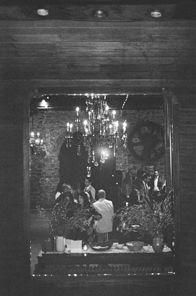 Black and white film photo of guests mingling inside Miners Foundry during cocktail hour.