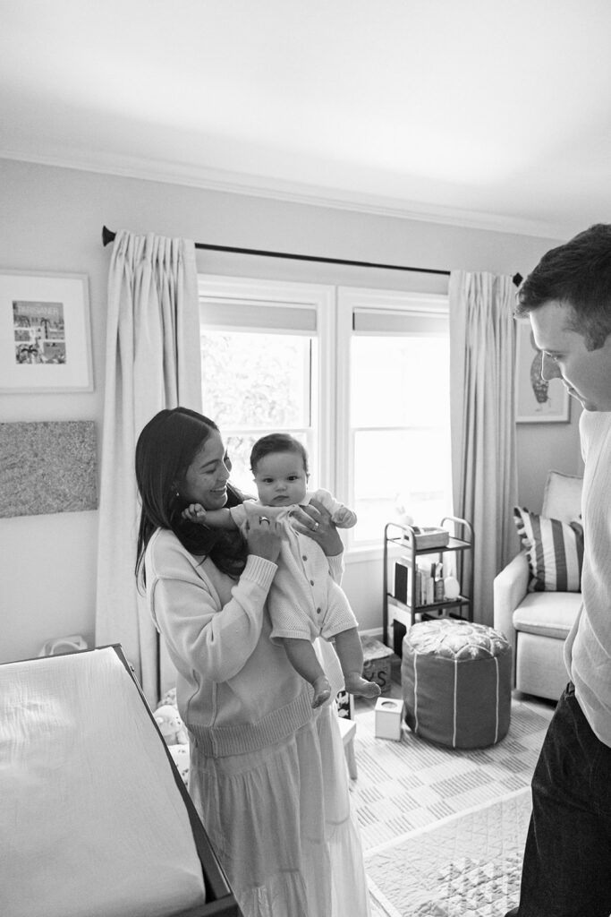 Black and white photo of a mother holding her baby in the nursery with the father nearby.