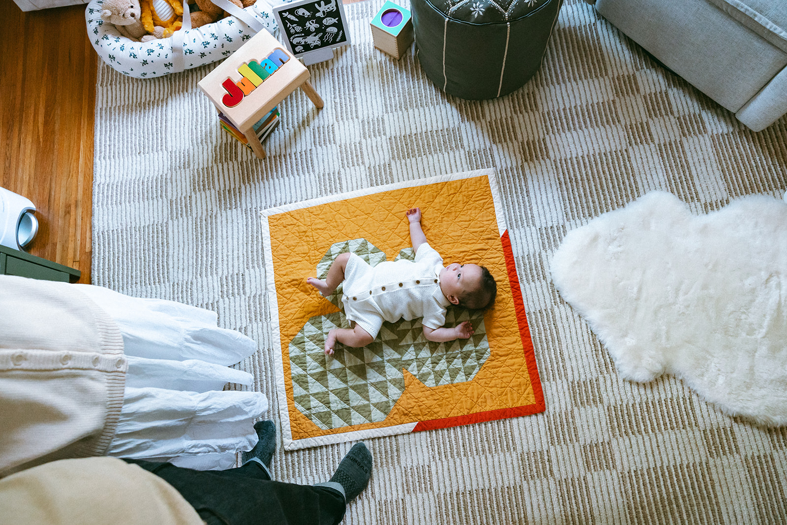 Wide shot of a baby laying on a quilt in his nurser with his parent standing close by. 
