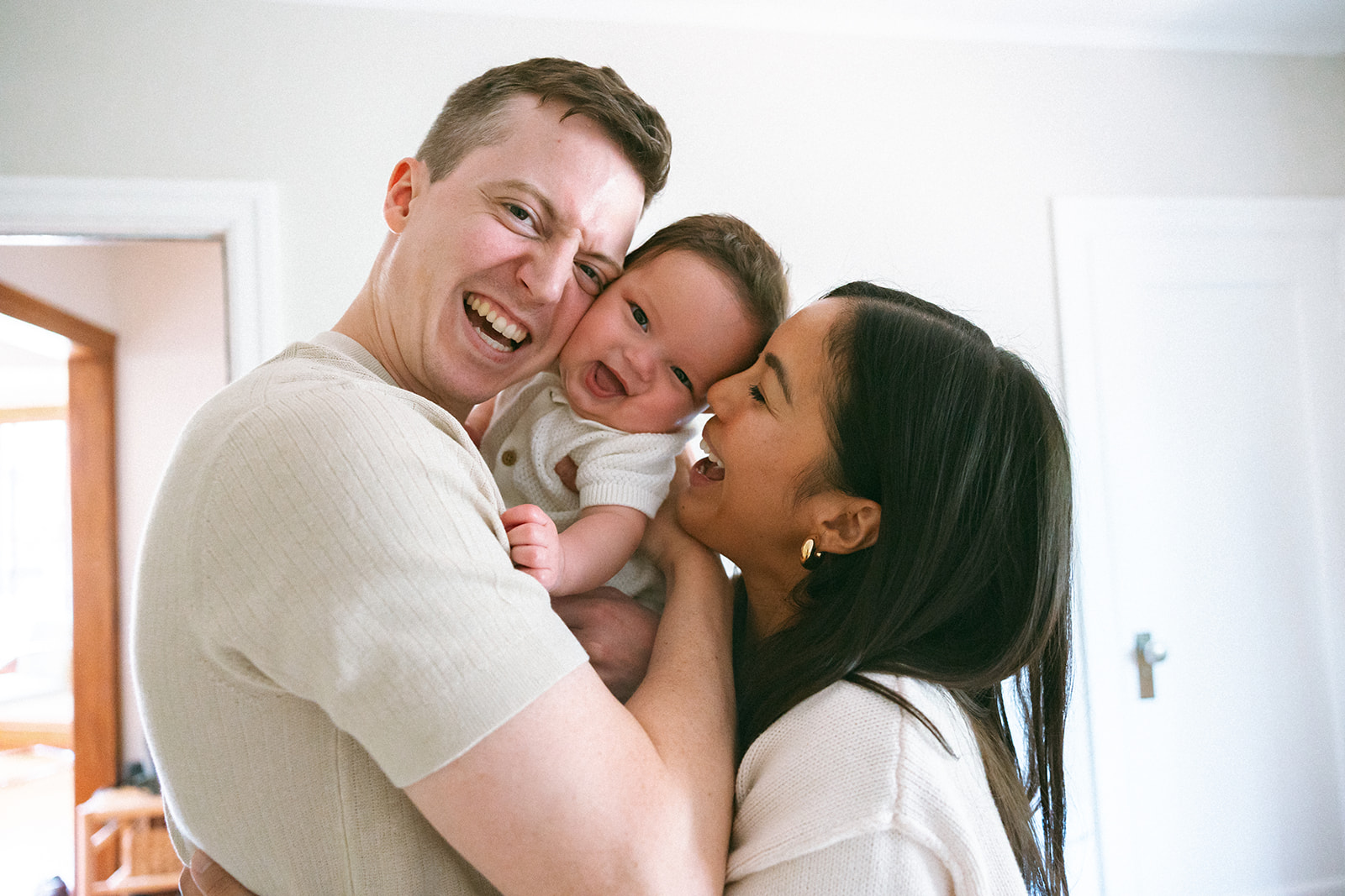 Mother and father laughing as they hold their baby in-between them.