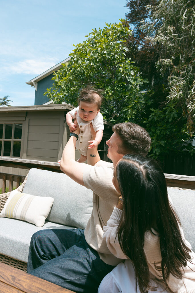 Family of three sitting on their patio with their baby for their at-home family photos in Oakland, California. 